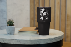 a black cup sitting on top of a table next to a plant