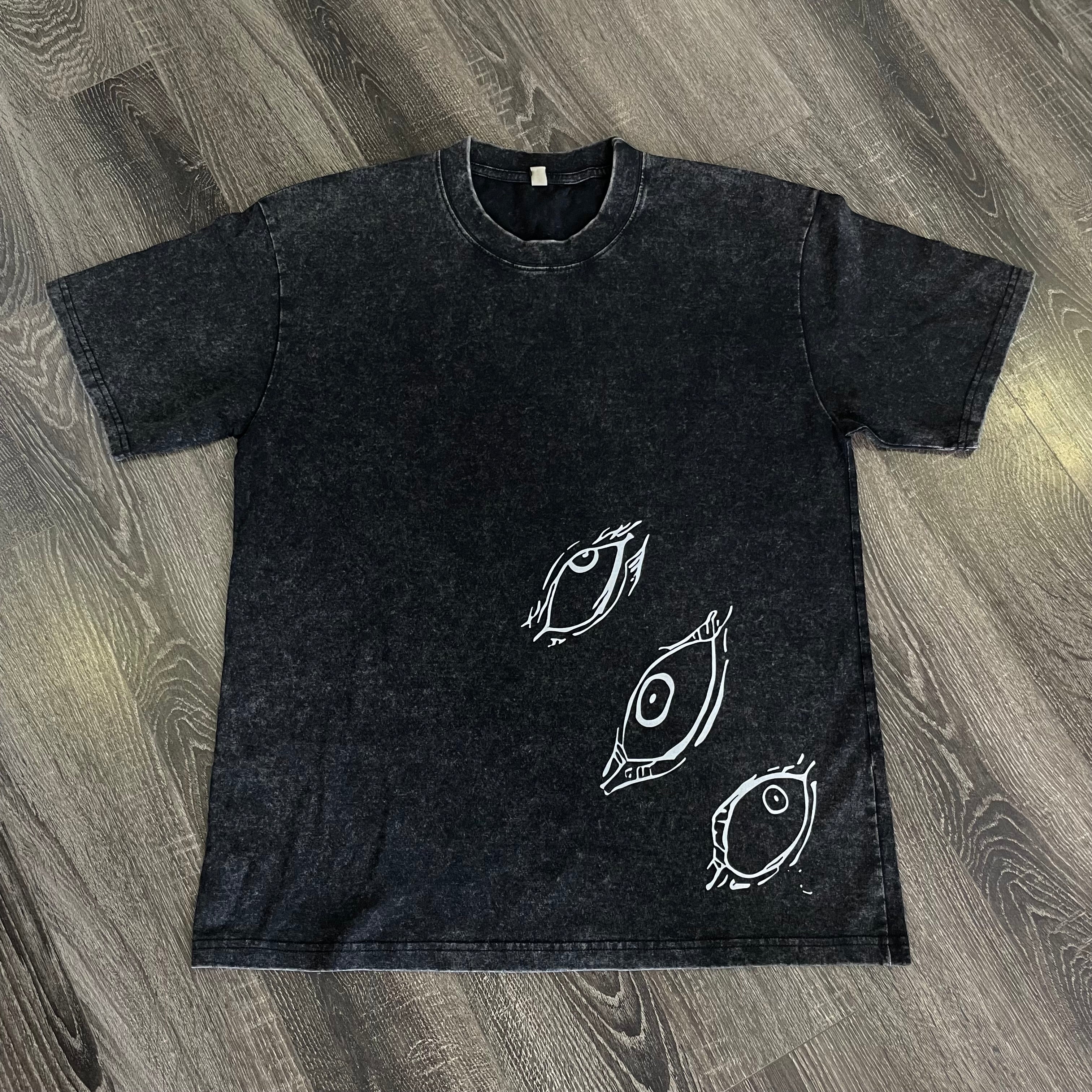 Black t-shirt with white fish illustrations on a wooden surface